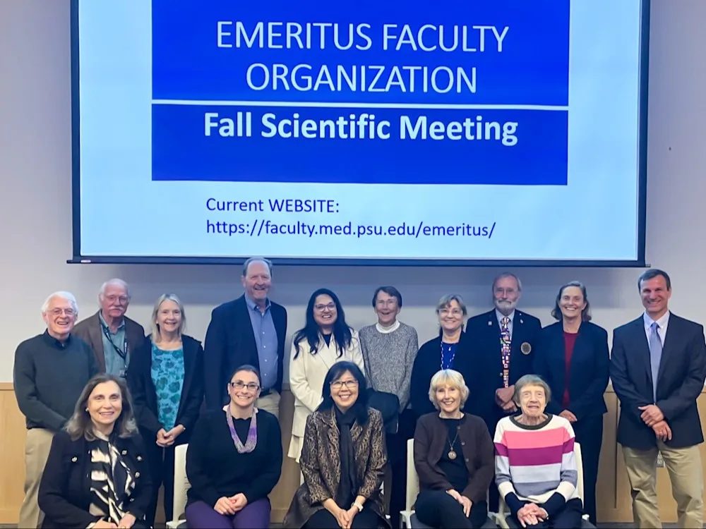 Group of 15 people, including Dean Karen Kim, in front of a screen with Emeritus Faculty Organization Fall Scientific Meeting