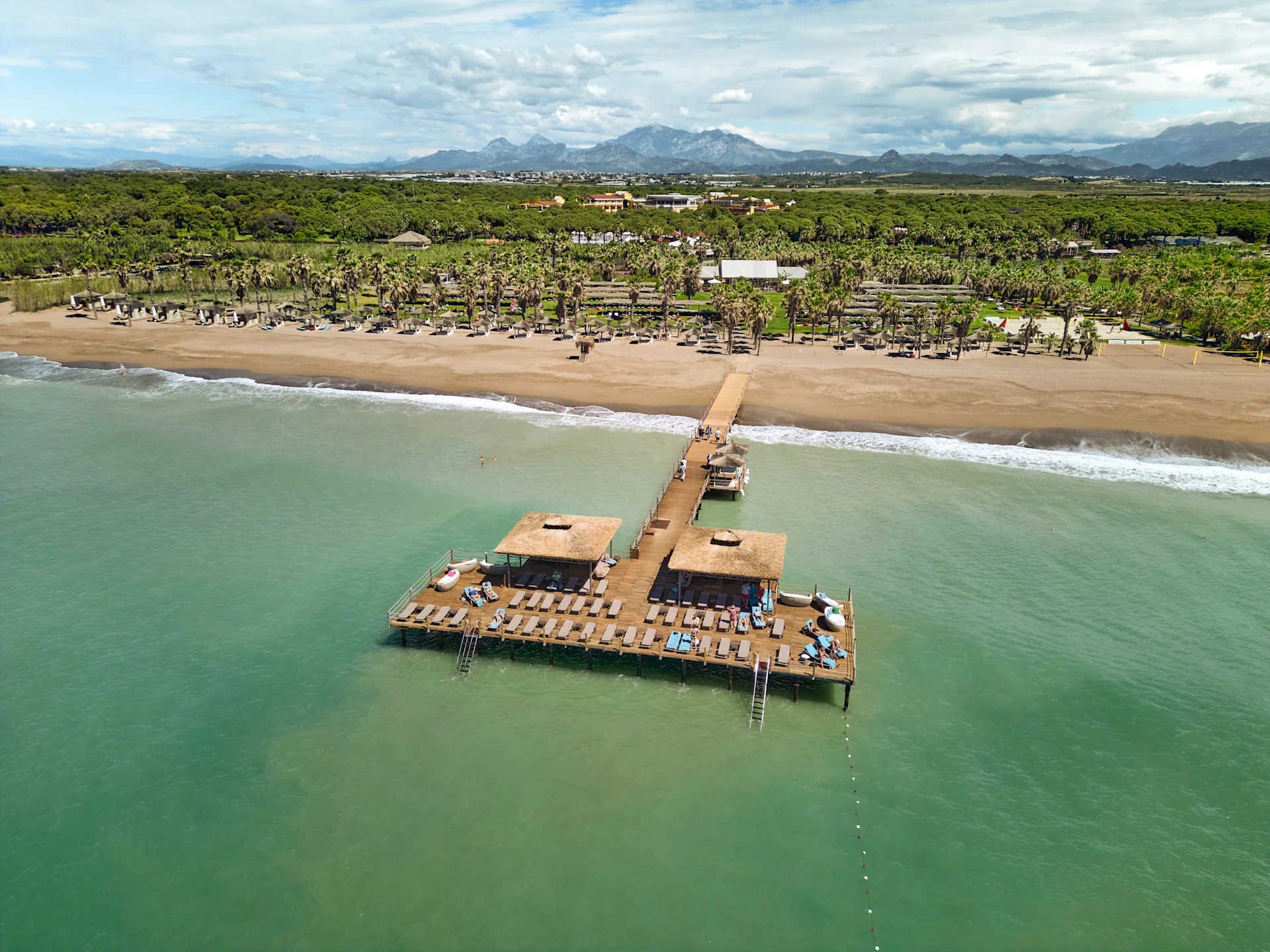 A view from above of the beach and the jetty at ROBINSON NOBILIS, with the mountains in the background