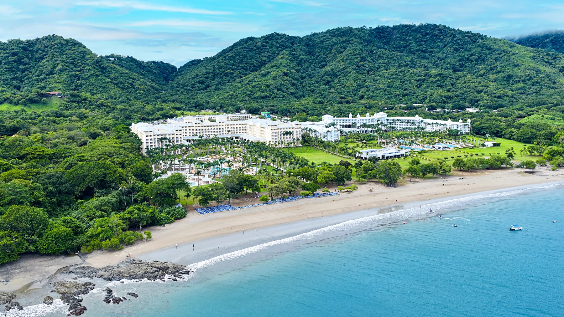 Aerial view of the beachfront resort Riu Guanacaste surrounded by tropical hills, palm gardens and turquoise waters.