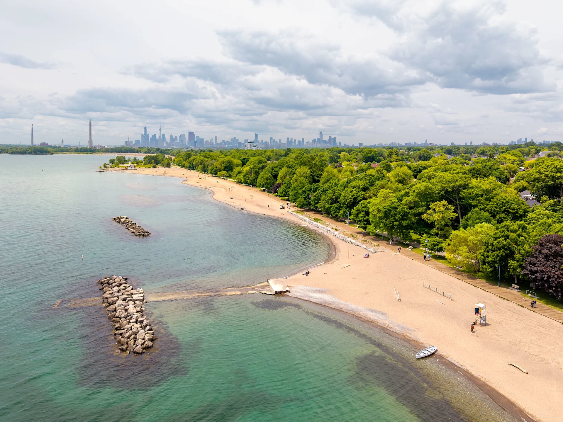 Aerial view of Woodbine Beach with clear water, sandy shoreline, green parkland, and the Toronto skyline in the distance