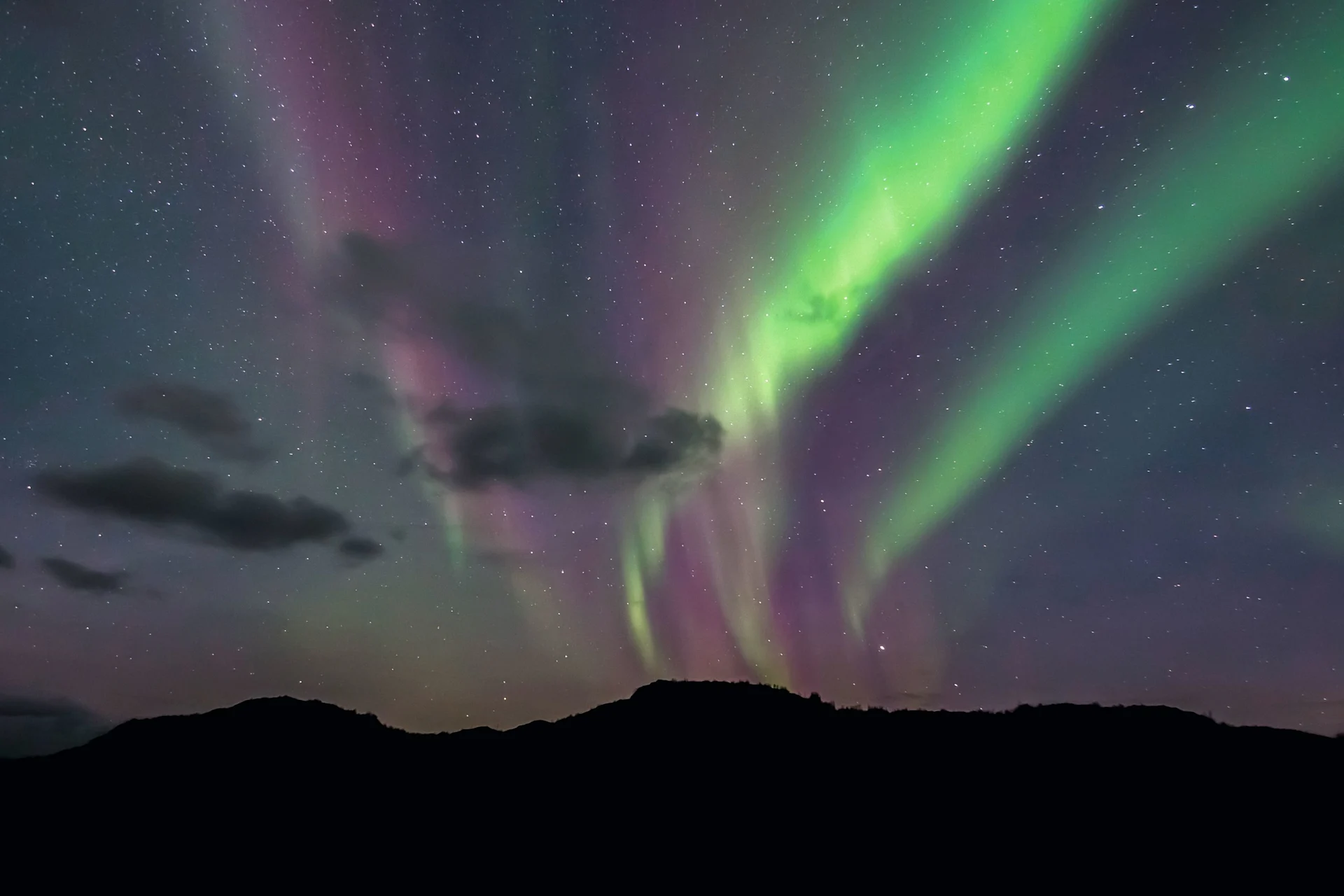 Aurora borealis with green and purple lights streaking across a starry night sky above dark hills