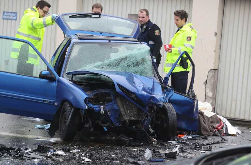 Rettungskräfte und Polizisten stehen um ein frontal verunglücktes Auto herum.