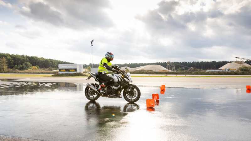 Dirk fährt auf rote Warnkegel zu und bremst sein Motorrad auf nassem Untergrund. 