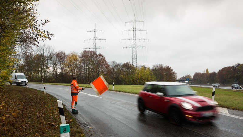Der Straßenwärter steht in einer Kurve einer Autobahnauffahrt und schwenkt eine orangene Flagge, um auf sich aufmerksam zu machen.