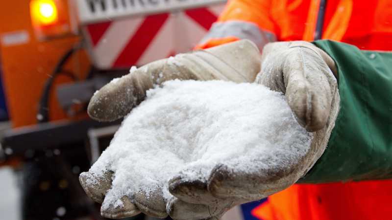 Ein Mitarbeiter des BSR-Winterdienstes hält Natriumchlorid in seinen Händen mit Handschuhen.