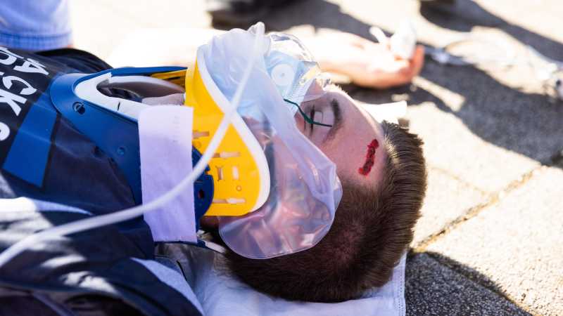 Ein verwundeter Mann liegt mit einer geschminkten Kopfverletzung am Boden. Er trägt ein Beatmungsgerät.