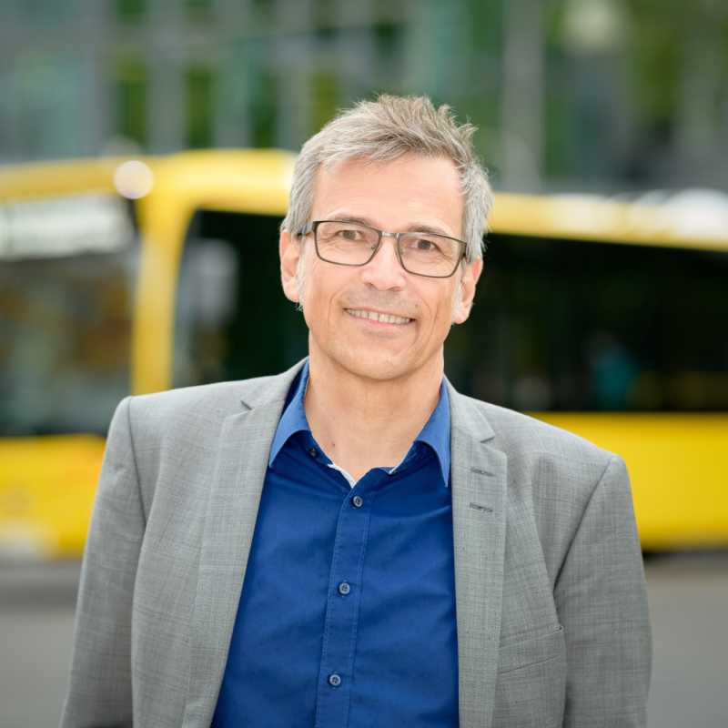 Ein Mann lächelt in die Kamera. Es ist Josef Weiß von der Deutschen Verkehrswacht. Im Hintergrund ist ein gelber Bus zu sehen.