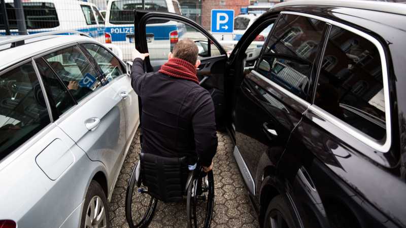 Ein Mann im Rollstuhl steigt auf der Fahrerseite seines Autos ein.