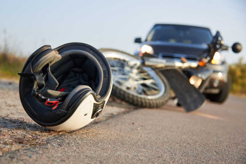 Ein weißer Helm und ein verunfalltes Motorrad liegen vor einem Pkw auf der Straße.