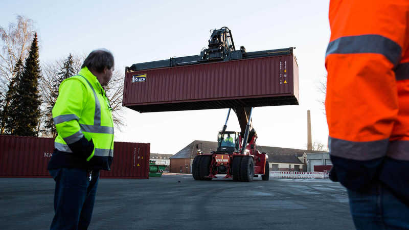Der Container für den LKW wird mit einem Kranwagen zum LKW transportiert.