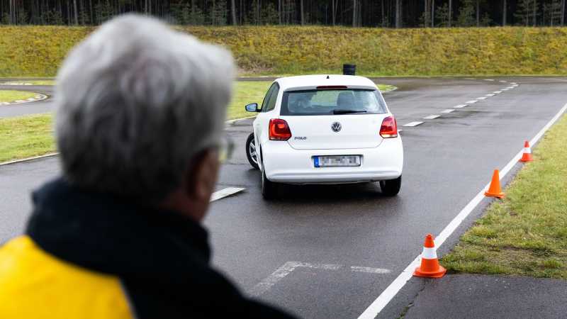 Ein Fahrtrainer beobachtet ein weißes Auto beim Einparken.