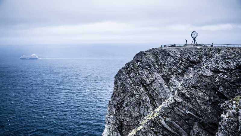 Das Nordkap an der norwegischen Küste. Mike reißt nach seiner Ankunft die Arme hoch. Im Hintergrund fährt eine Fähre.