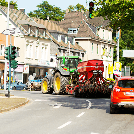 Ein Traktor mit Pflügwerkzeug biegt innerhalb einer Ortschaft ab.
