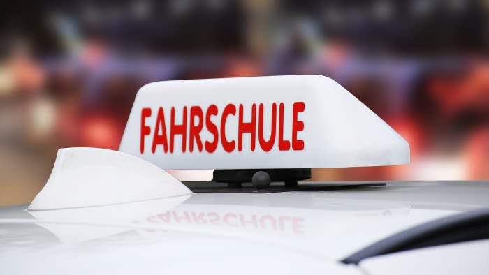 Ein Fahrschulschild auf dem Dach eines weißen Pkw.  