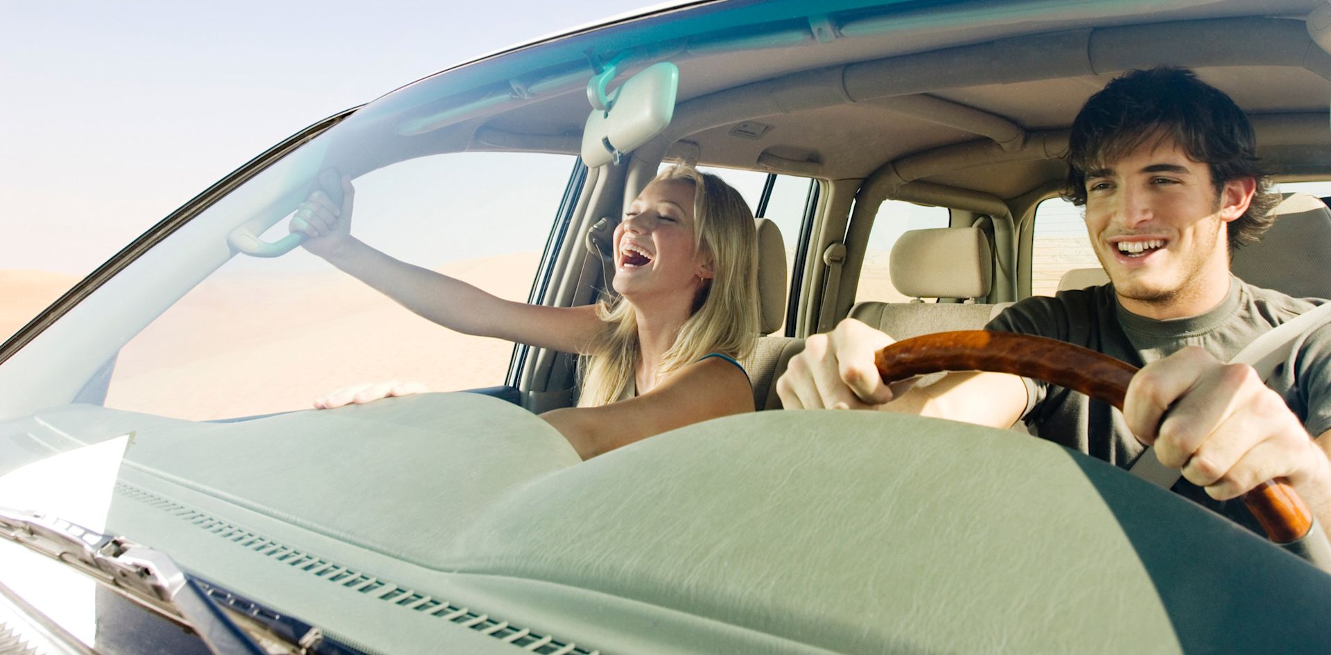 Eine junge Frau und ein junger Mann sitzen lachend im Auto. 