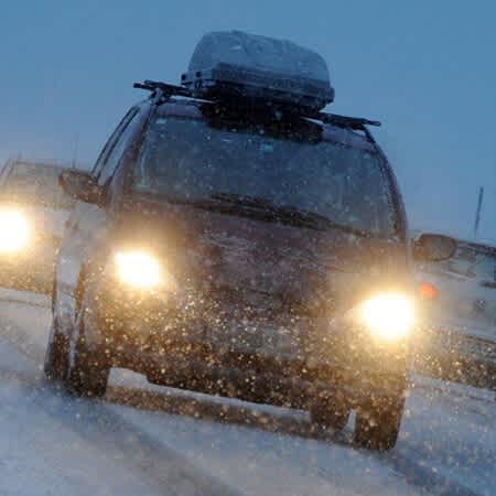 Autos fahren in der Dämmerung auf einer schneebdeckten Straße.