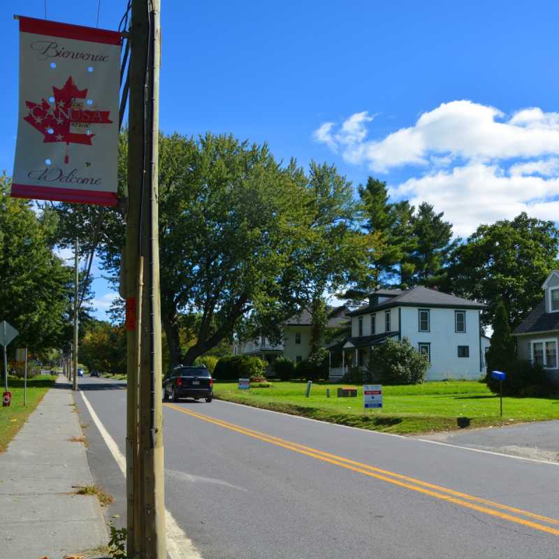 Längs einer Straße ist eine doppelte gelbe Linie gezogen. Im Vordergrund ist die Flagge Kanadas erkennbar. 