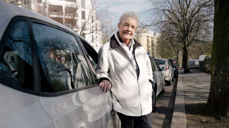 Seniorin Ursula Kraus steht neben ihrem silbernen Auto.