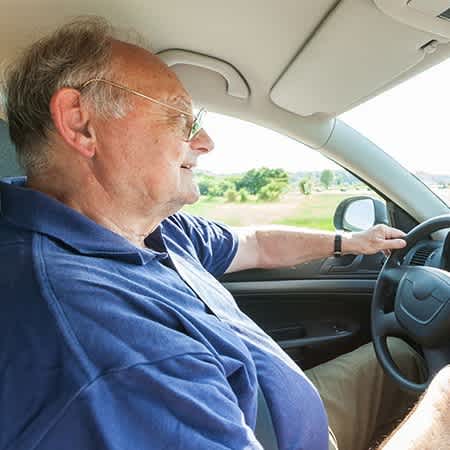 Ein älterer Mann sitzt am Steuer und fährt Auto.
