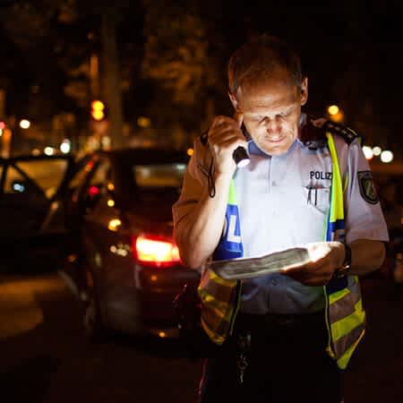 Polizist Rainer Fuchs prüft die Genehmigungen des angehaltenen Autos mit einer Taschenlampe.