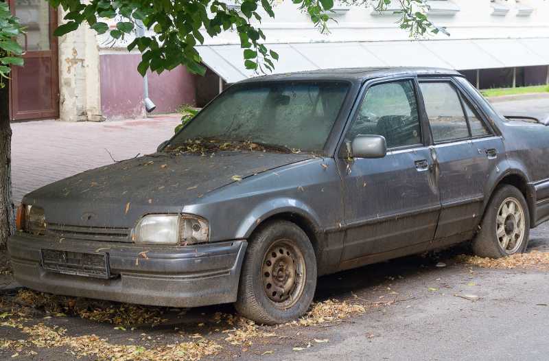 Das Bild zeigt ein verwahrlostes Auto am Straßenrand.