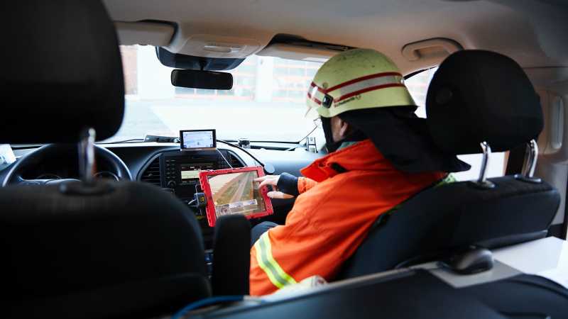 Eine Feuerwehrmann sitzt in einem Einsatzfahrzeug und blickt auf ein Tablet. 