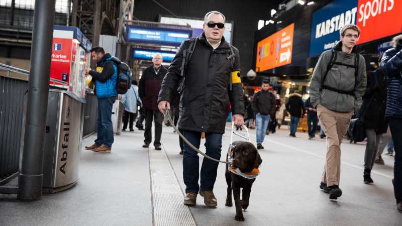 Das Bild zeigt Andreas Schmelt im Hamburger Hauptbahnhof zusammen mit seinem Blindenhund.