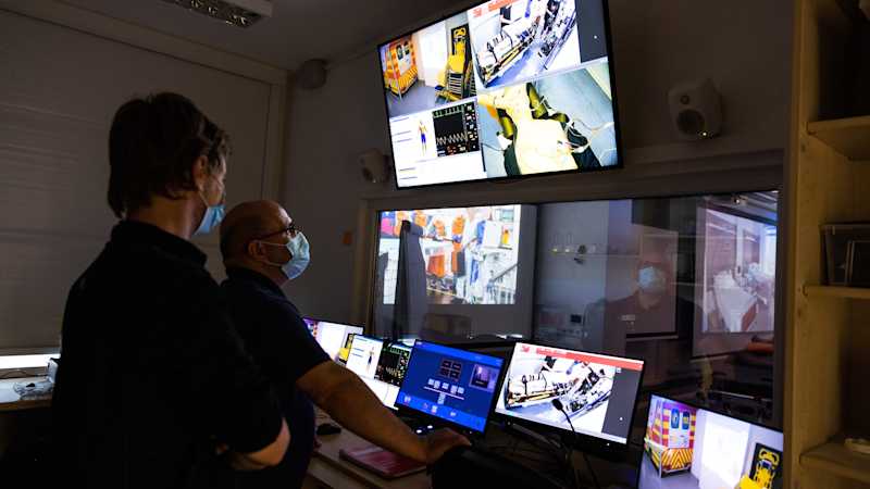 Zwei Männer stehen vor vielen Bildschirmen. Beide beobachten per Kamera die Übung der Schüler im Simulationszentrum.