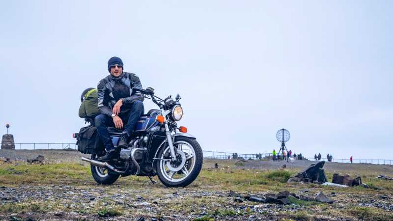 Mike Dodd sitzt am Nordkap auf seinem Motorrad und blickt in die Kamera.