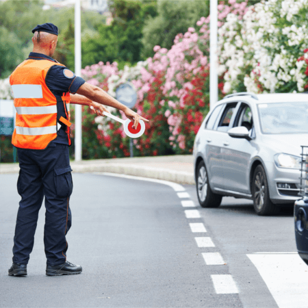 Ein Verkehrspolizist mit Warnweste weißt Autos den Weg in einer mediterranen Umgebung.