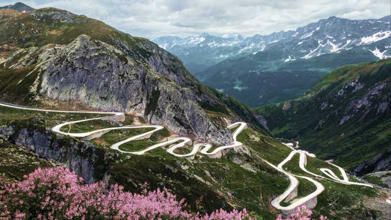 Das Bild zeigt zeigt die Gotthardpasstraße mit den Alpen im Hintergrund.