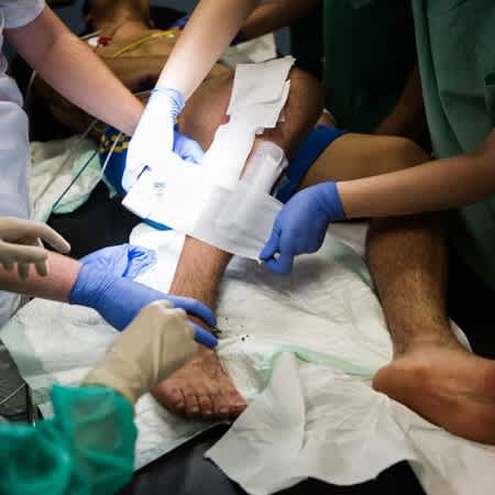 Mehrere Leute verbinden eine Verletzung am Bein eines Patienten.