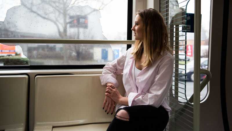 Das Bild zeigt eine junge Frau, die alleine in der Bahn sitzt und aus dem Fenster schaut.