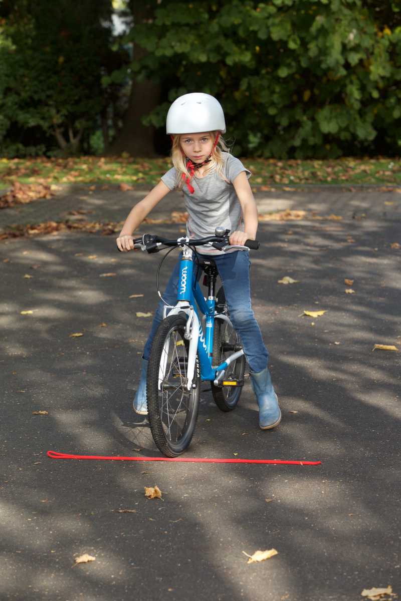 Ein Kind auf einem Fahrrad befindet sich vor einem auf dem Boden hingelegten Seil.