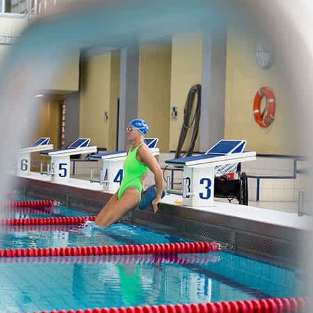 Kirsten Bruhn in neongrünem Badeanzug gleitet ins Wasser des Schwimmbeckens.