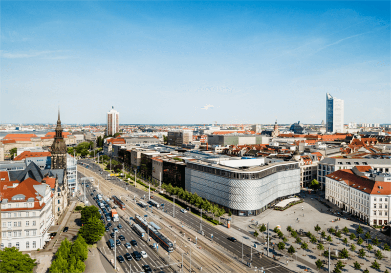 Das Bild zeigt eine Luft-Aufnahme von Leipzig. Zu sehen sind eine Straße, auf der viele Autos fahren. Im Hintergrund sieht man viele Häuser.