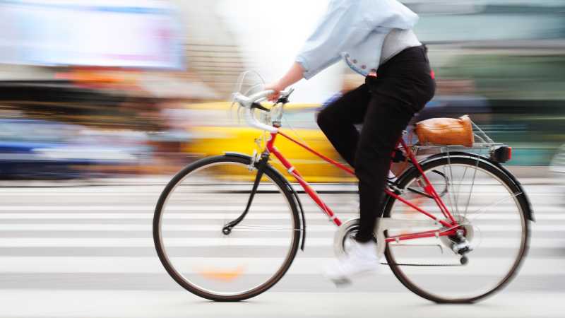 Eine Person fährt in der Stadt auf einem roten Fahrrad mit hoher Geschwindigkeit, der Hintergrund ist verschwommen.