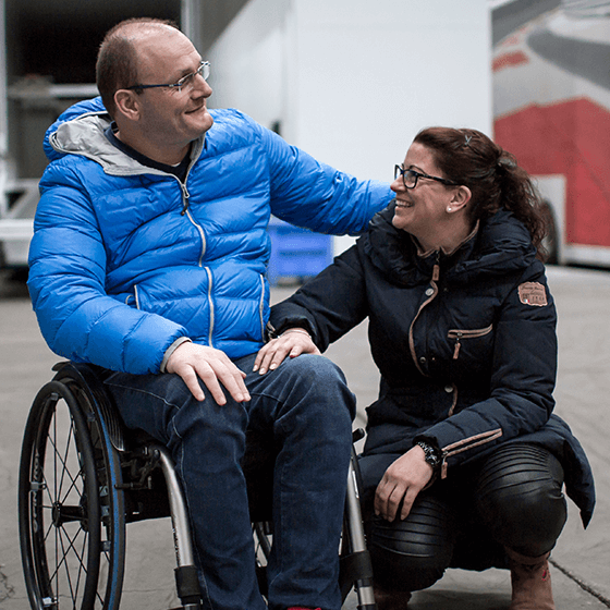 Gustav Engljähringer sitzt im Rollstuhl und seine Frau kniet neben ihm.