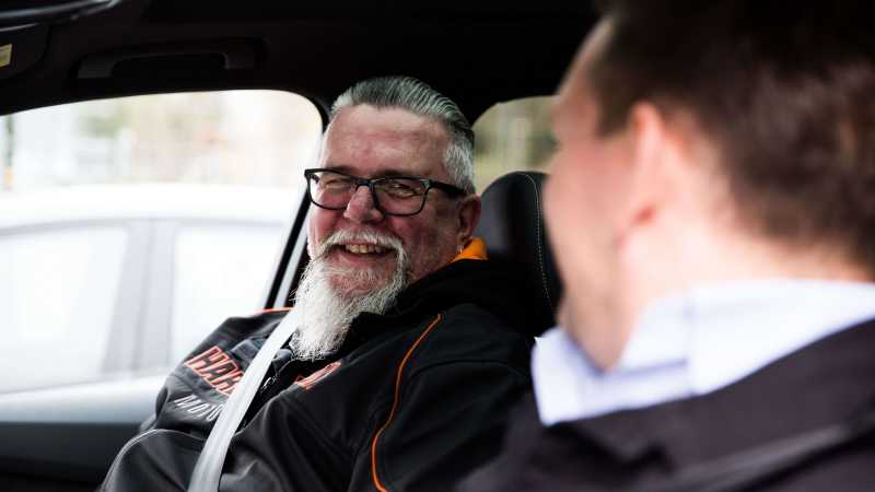 Ein Mann sitzt auf dem Beifahrersitz und lächelt dem Fahrer zu.