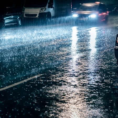 Man sieht Starkregen auf einer Straße, auf der ein Auto fährt.