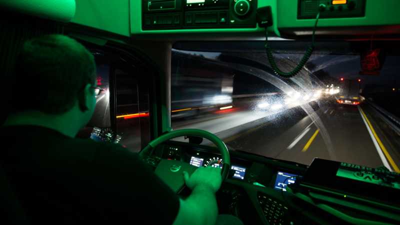 Der Sohn sitzt in der Fahrerkabine seines LKWs, die in grünes Licht getaucht ist.