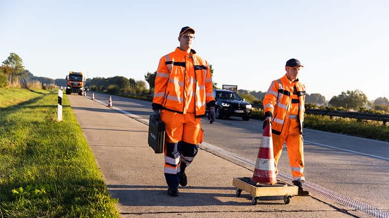 Zwei Straßenwärter stellen Leitkegel auf dem Seitenstreifen auf.