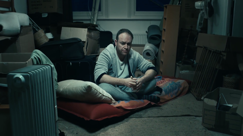 Der Protagonist Brandon sitzt zwischen Müll und Gerümpel auf einer Matratze auf dem Boden.