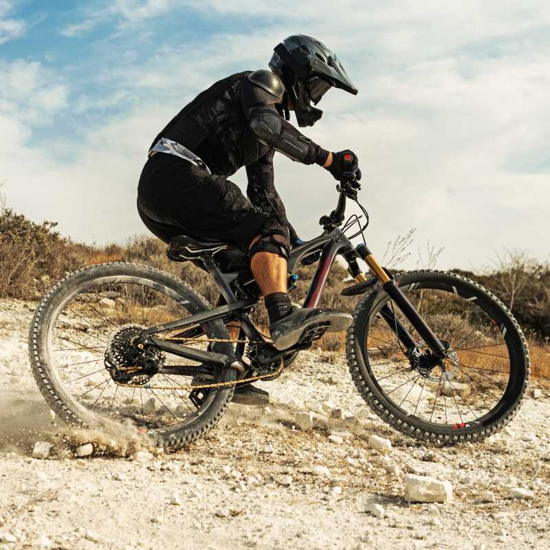 Ein Downhill-Fahrer schlittert eine sandige Piste hinab und trägt einen Fullface-Helm. 