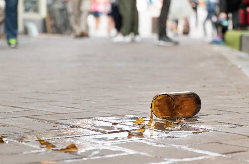Eine zerbrochene braune Flasche liegt auf einer gepflasterten Straße. 