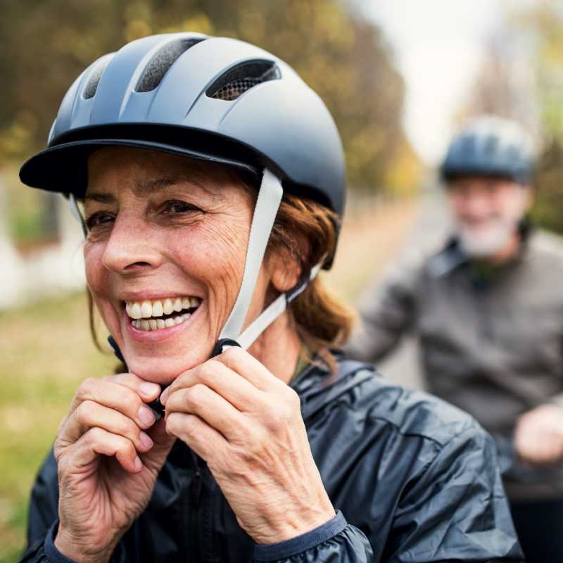 Eine Frau mit braunen Haaren setzt sich einen schwarzen Fahrradhelm auf.