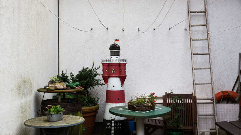 Ein Miniatur-Leuchtturm steht umgeben von Tischen und Pflanzen vor einer Wand.