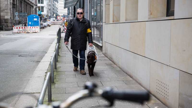 Das Bild zeigt Andreas und seinen Hund Henri auf einem Gehweg.
