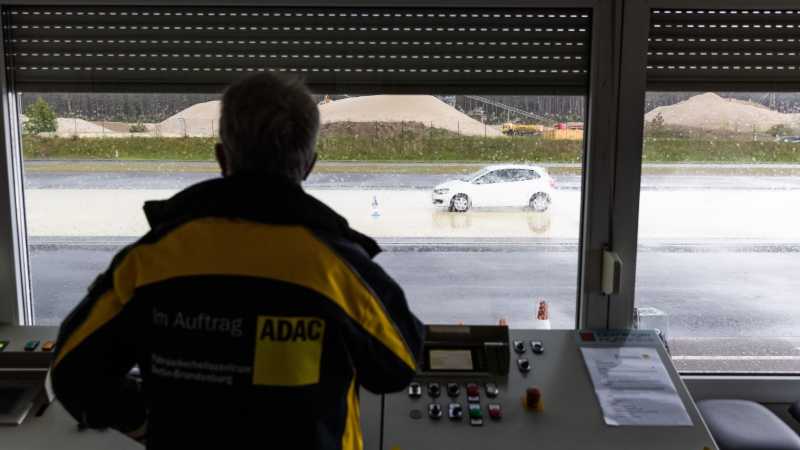 Im Vordergrund steht der Fahrtrainer Jürgen Dörfler. Er beobachtet ein weißes Auto. 