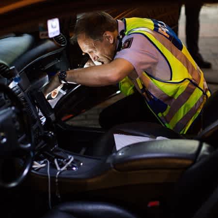 Polizist Rainer Fuchs überprüft die Beifahrerseite eines getunten Autos mit einer Taschenlampe.